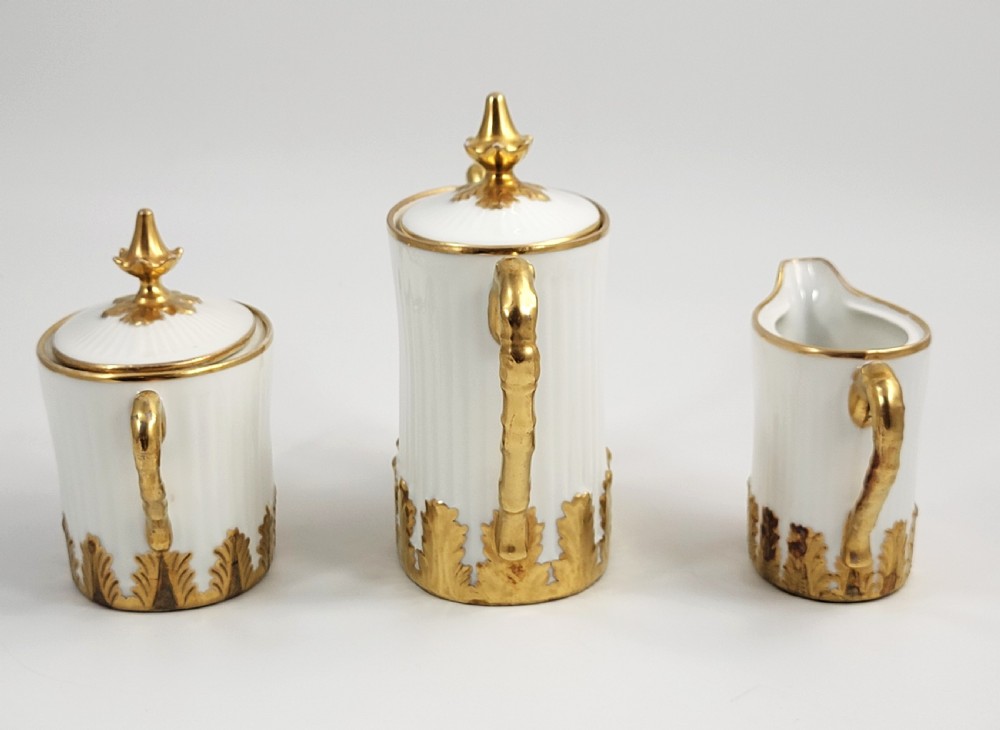A three-piece white porcelain coffee set featuring a pot, sugar bowl, and cream jug with fluted bodies and gilded acanthus leaf detailing. View II