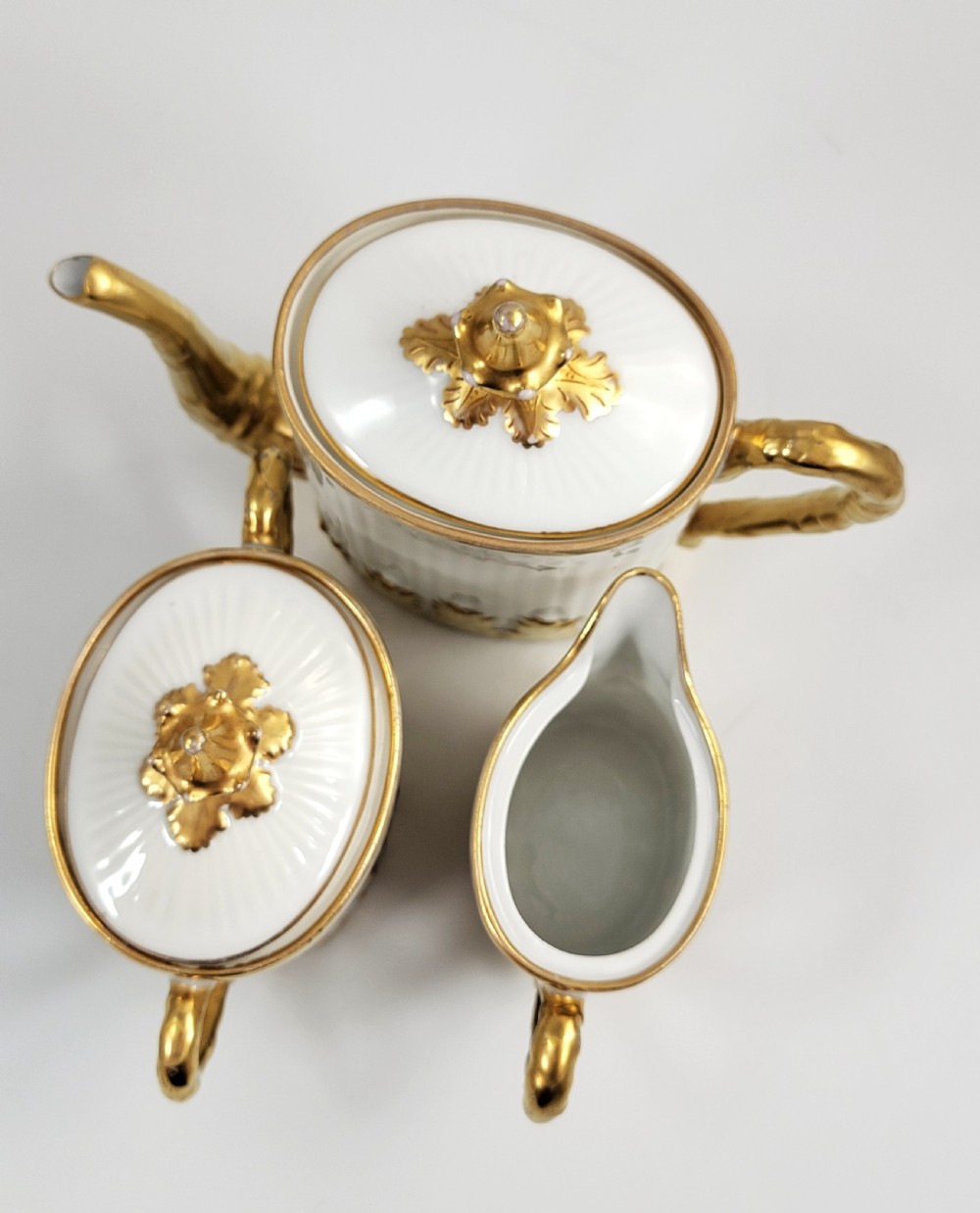 A three-piece white porcelain coffee set featuring a pot, sugar bowl, and cream jug with fluted bodies and gilded acanthus leaf detailing. View VI