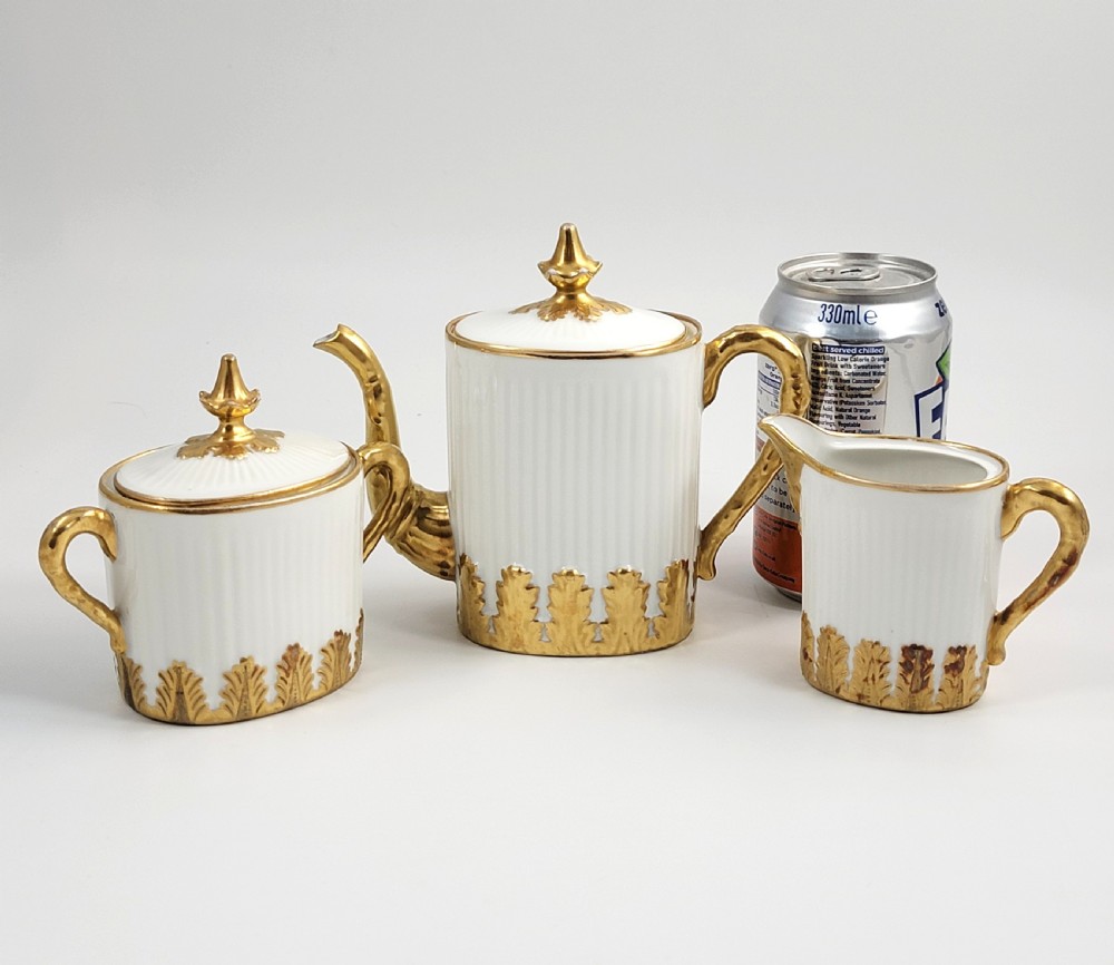 A three-piece white porcelain coffee set featuring a pot, sugar bowl, and cream jug with fluted bodies and gilded acanthus leaf detailing. View XIII