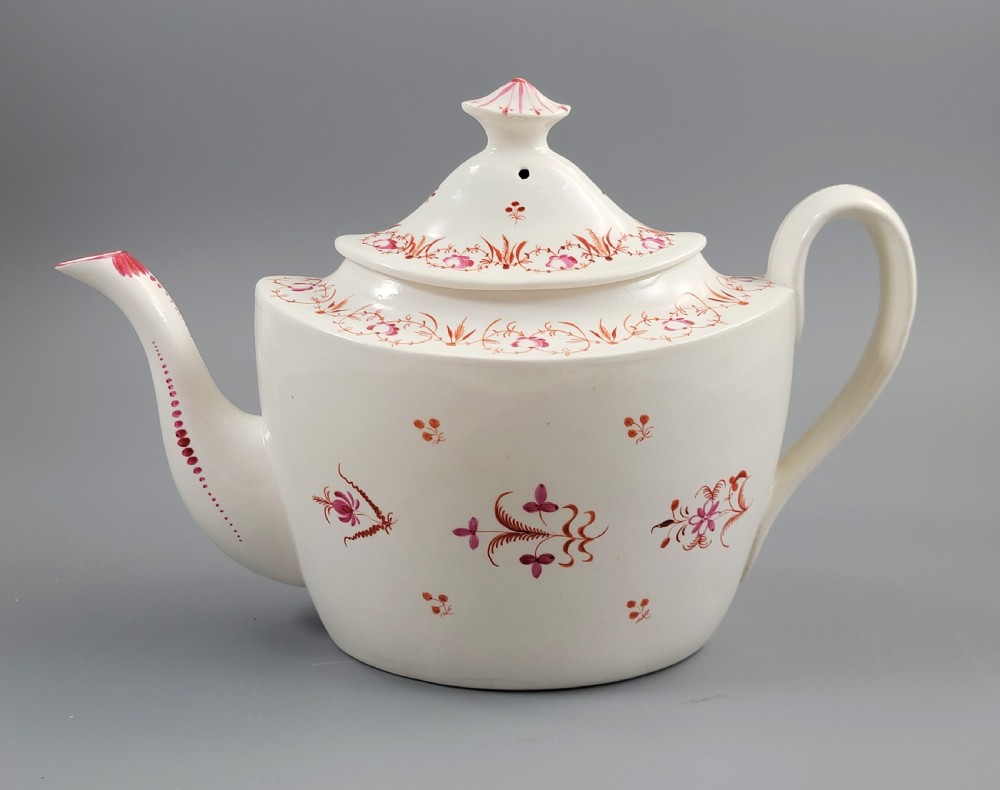 A cream-coloured Georgian porcelain teapot decorated with hand-painted reddish-pink floral sprigs, featuring a high lid with a knop and a curved spout.