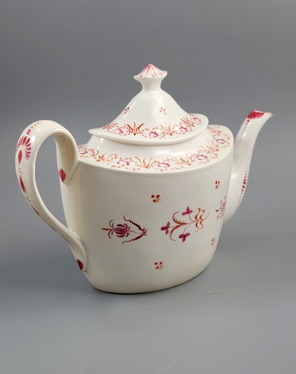 A cream-coloured Georgian porcelain teapot decorated with hand-painted reddish-pink floral sprigs, featuring a high lid with a knop and a curved spout. View III