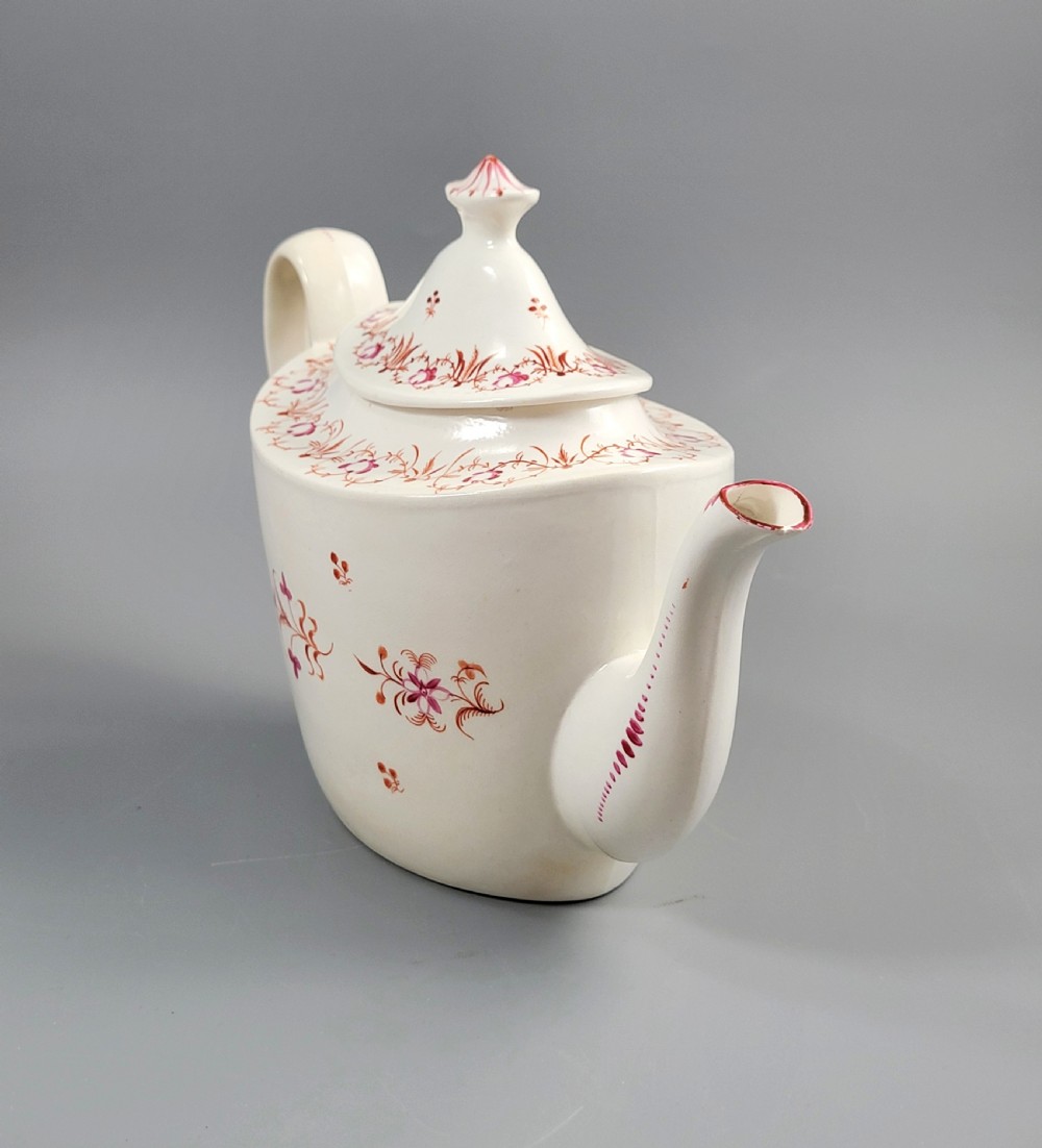A cream-coloured Georgian porcelain teapot decorated with hand-painted reddish-pink floral sprigs, featuring a high lid with a knop and a curved spout. View V