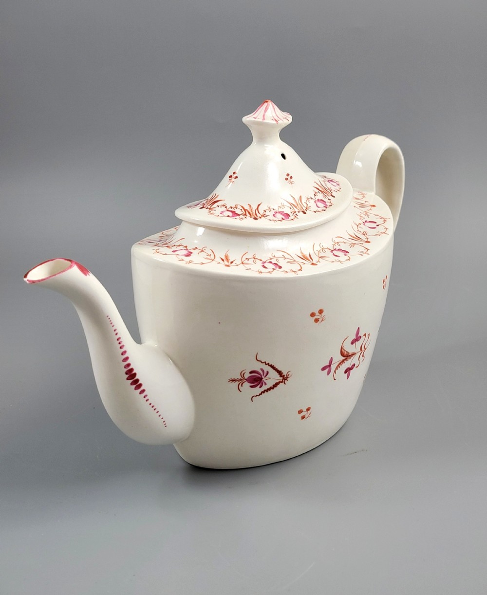 A cream-coloured Georgian porcelain teapot decorated with hand-painted reddish-pink floral sprigs, featuring a high lid with a knop and a curved spout. View VI
