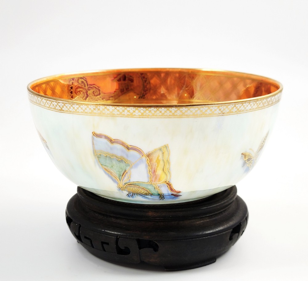 A rounded ceramic lustreware bowl featuring polychrome butterfly illustrations on an iridescent white exterior and an orange gilded interior.
