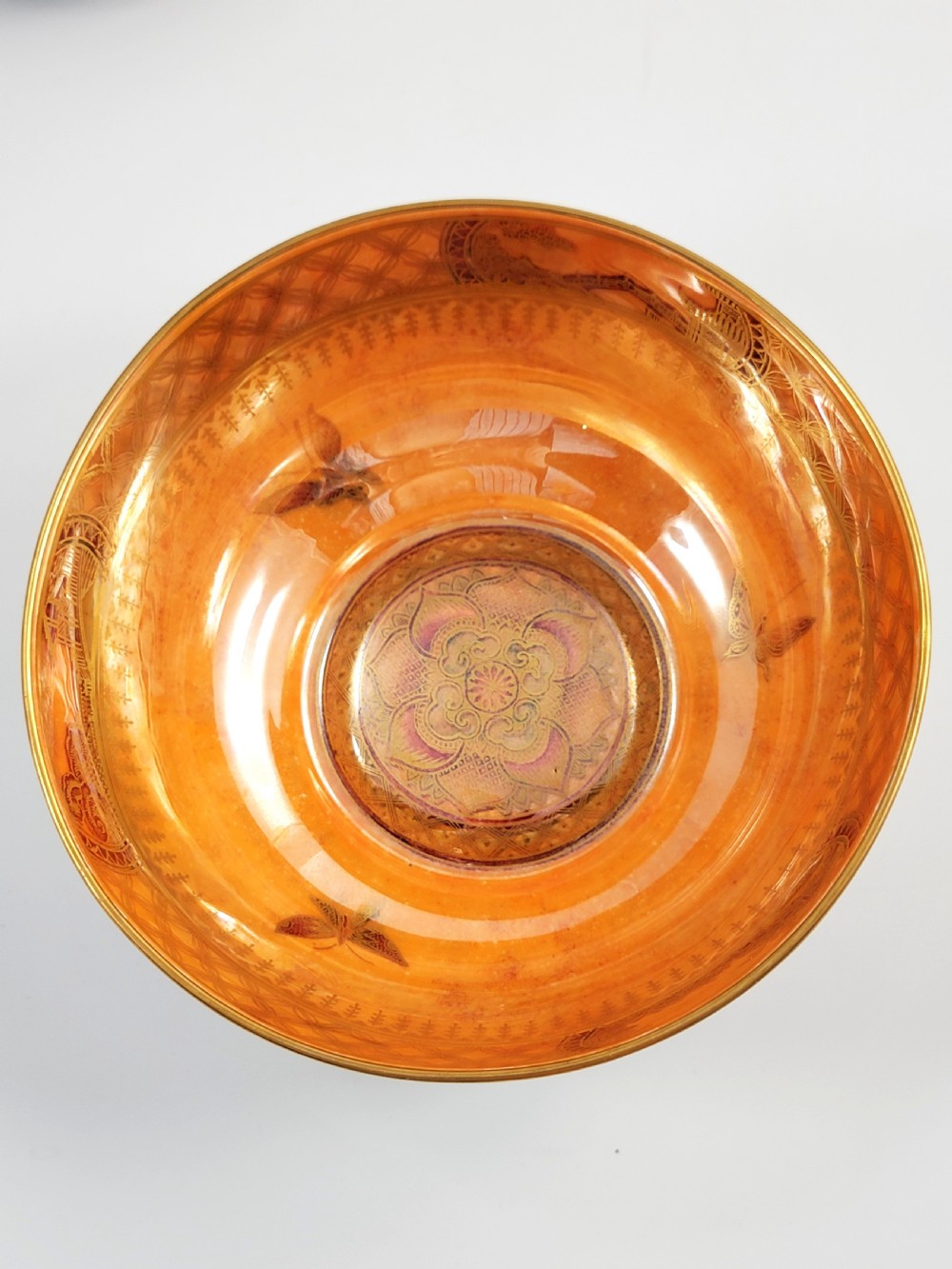 A rounded ceramic lustreware bowl featuring polychrome butterfly illustrations on an iridescent white exterior and an orange gilded interior. View VII