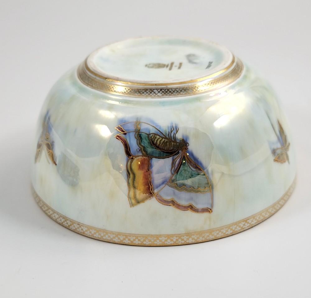 A rounded ceramic lustreware bowl featuring polychrome butterfly illustrations on an iridescent white exterior and an orange gilded interior. View X