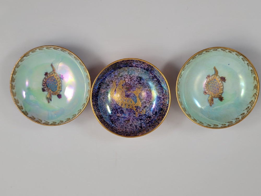 A set of three miniature footed porcelain bowls featuring iridescent lustre glazes in shades of blue, orange, and turquoise, embellished with gilded rim details and central motifs. View III