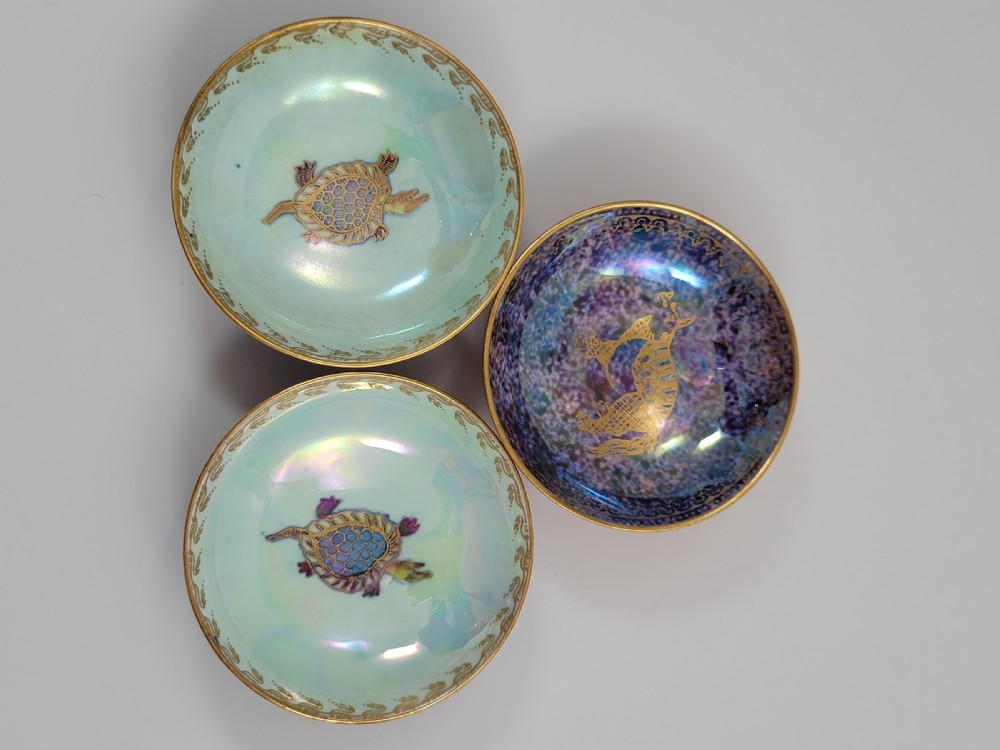 A set of three miniature footed porcelain bowls featuring iridescent lustre glazes in shades of blue, orange, and turquoise, embellished with gilded rim details and central motifs. View IV