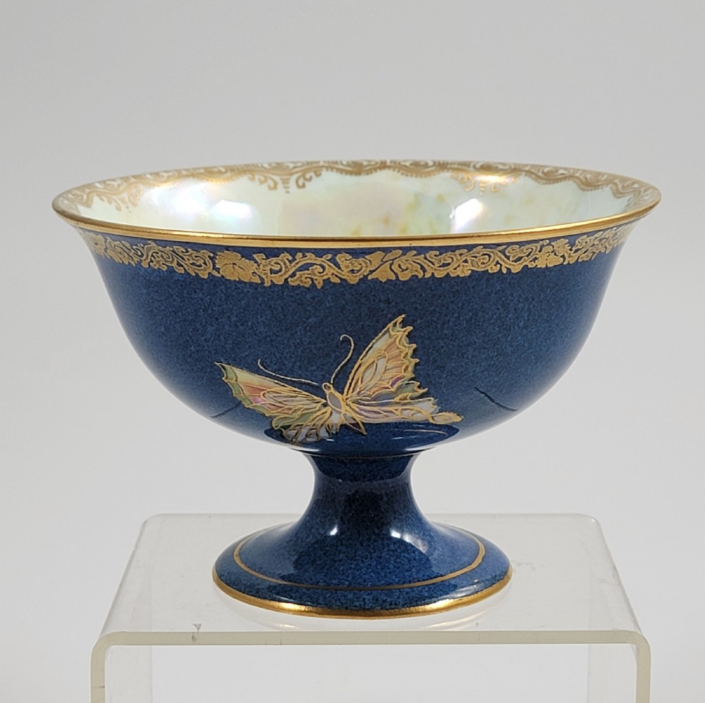 A footed Wedgwood porcelain bowl featuring a deep blue mottled exterior embellished with a gilded butterfly and an iridescent pearlescent interior with gold trim.