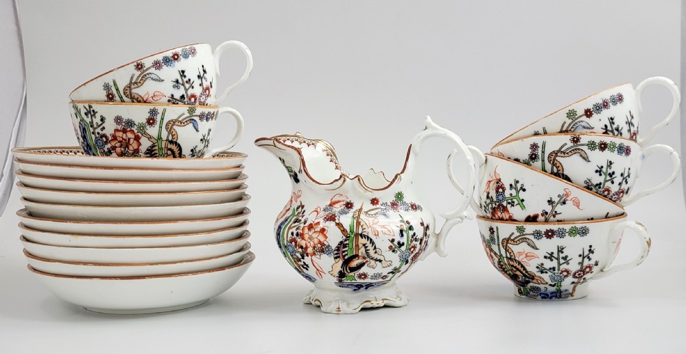 A Victorian Minton porcelain tea set featuring cups, stacked saucers, and a milk jug adorned with polychrome Kakiemon style tigers, bamboo, and flora.