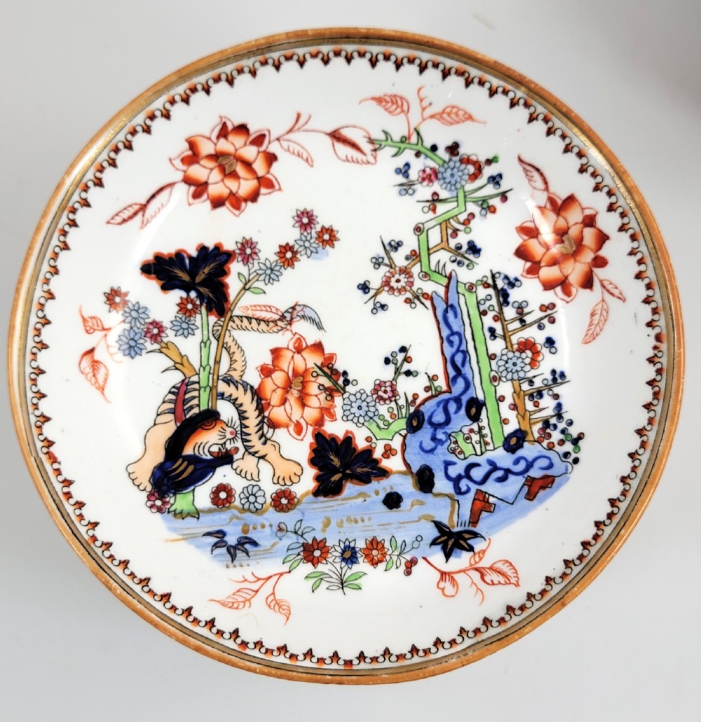 A Victorian Minton porcelain tea set featuring cups, stacked saucers, and a milk jug adorned with polychrome Kakiemon style tigers, bamboo, and flora. View II