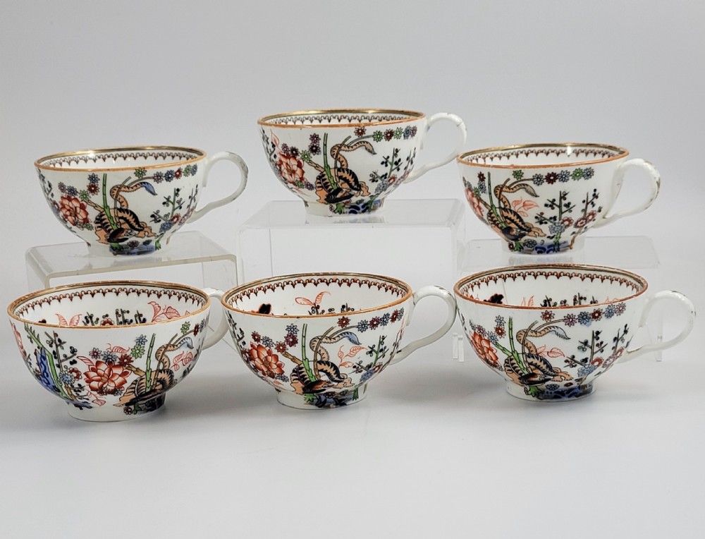 A Victorian Minton porcelain tea set featuring cups, stacked saucers, and a milk jug adorned with polychrome Kakiemon style tigers, bamboo, and flora. View XII