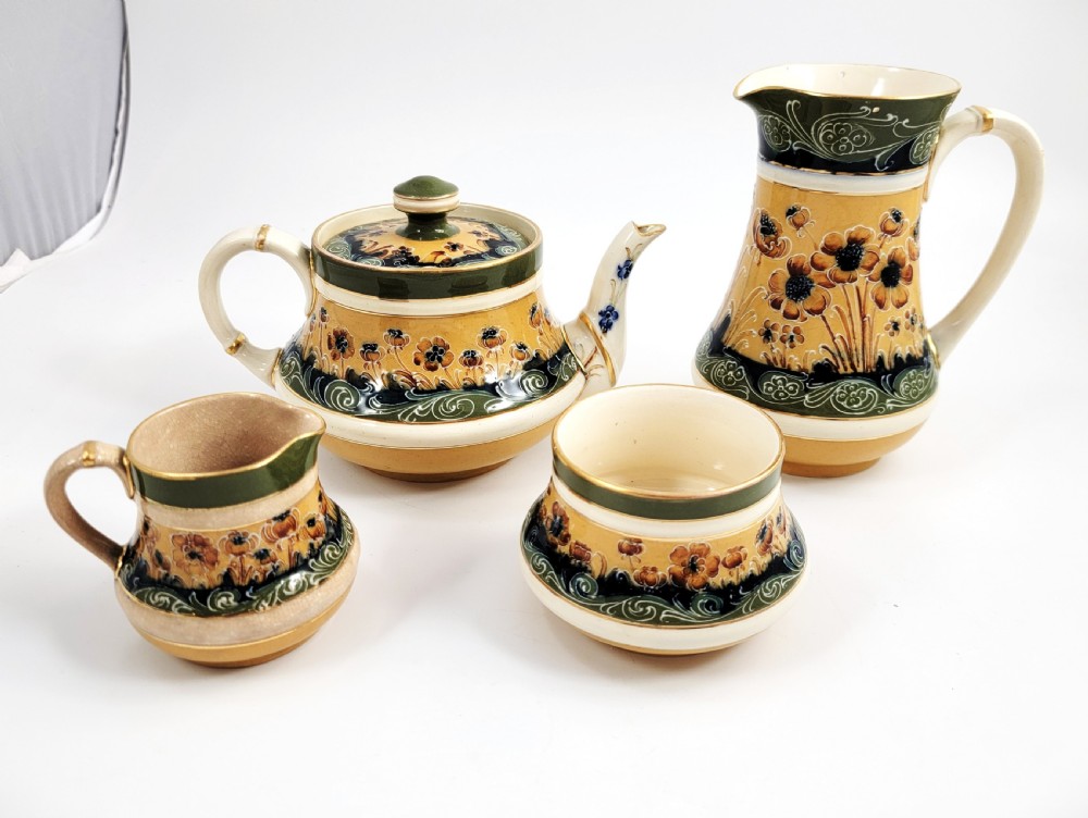 An antique four-piece Art Nouveau ceramic tea service decorated with tube-lined ochre poppy motifs and dark green glaze borders with gilded accents.