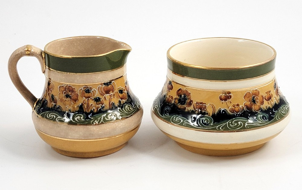 An antique four-piece Art Nouveau ceramic tea service decorated with tube-lined ochre poppy motifs and dark green glaze borders with gilded accents. View V