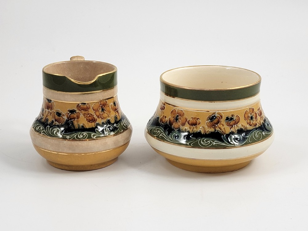 An antique four-piece Art Nouveau ceramic tea service decorated with tube-lined ochre poppy motifs and dark green glaze borders with gilded accents. View VI