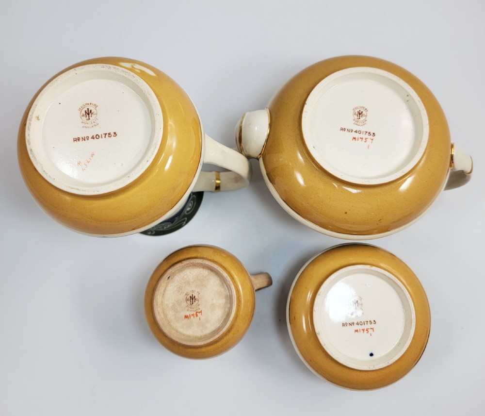 An antique four-piece Art Nouveau ceramic tea service decorated with tube-lined ochre poppy motifs and dark green glaze borders with gilded accents. View X