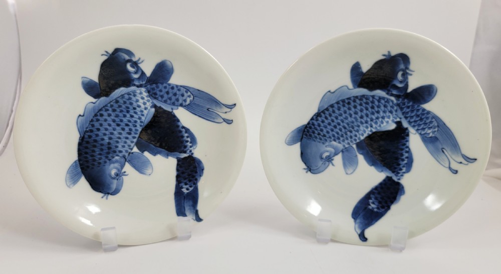 A near-pair of circular white Japanese porcelain plates decorated with hand-painted cobalt blue depictions of two koi fish.