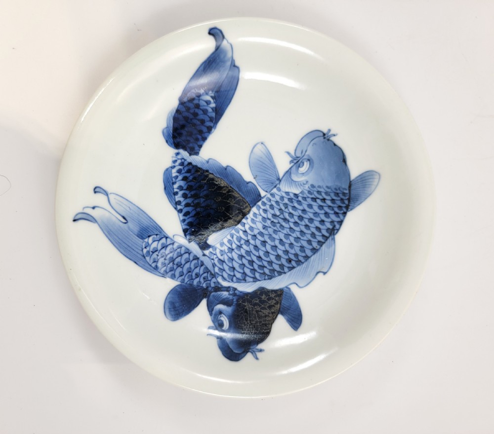 A near-pair of circular white Japanese porcelain plates decorated with hand-painted cobalt blue depictions of two koi fish. View VII