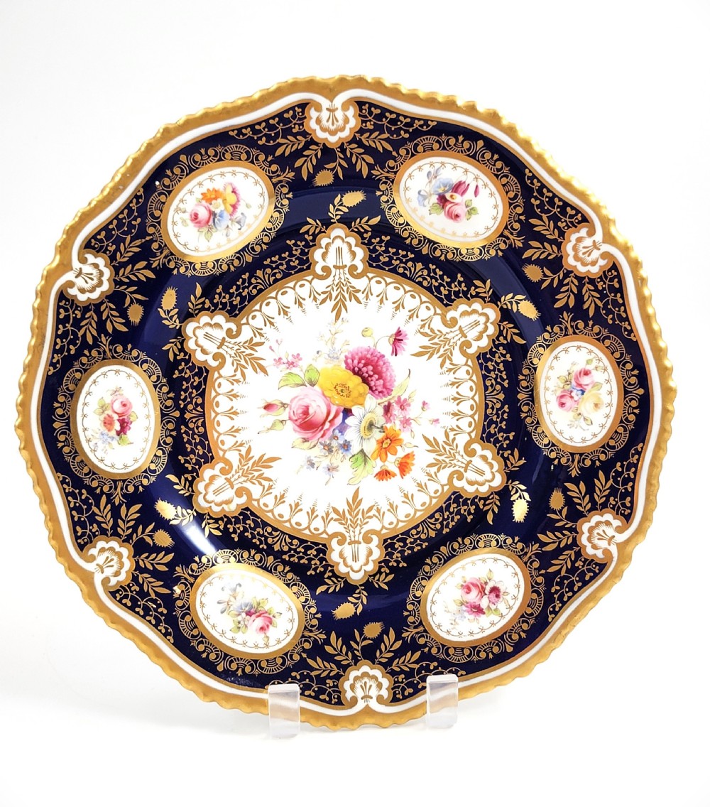 An Edwardian Royal Worcester circular porcelain cabinet plate with a cobalt blue rim decorated in heavy tooled gilding and six small floral cartouches surrounding a central hand-painted bouquet.