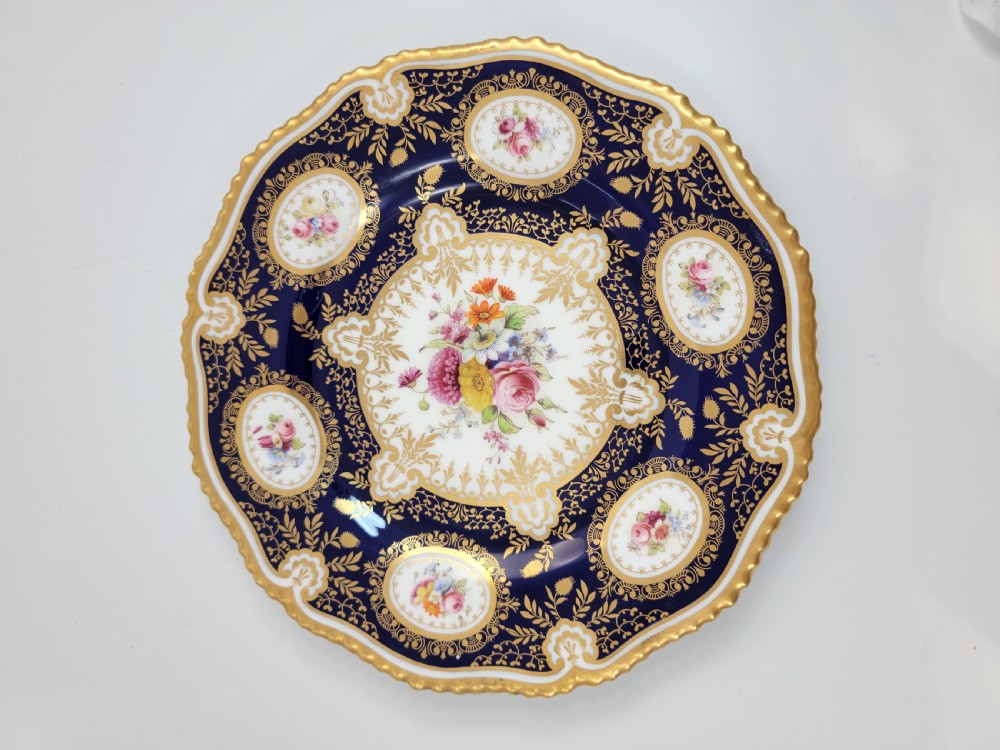 An Edwardian Royal Worcester circular porcelain cabinet plate with a cobalt blue rim decorated in heavy tooled gilding and six small floral cartouches surrounding a central hand-painted bouquet. View V