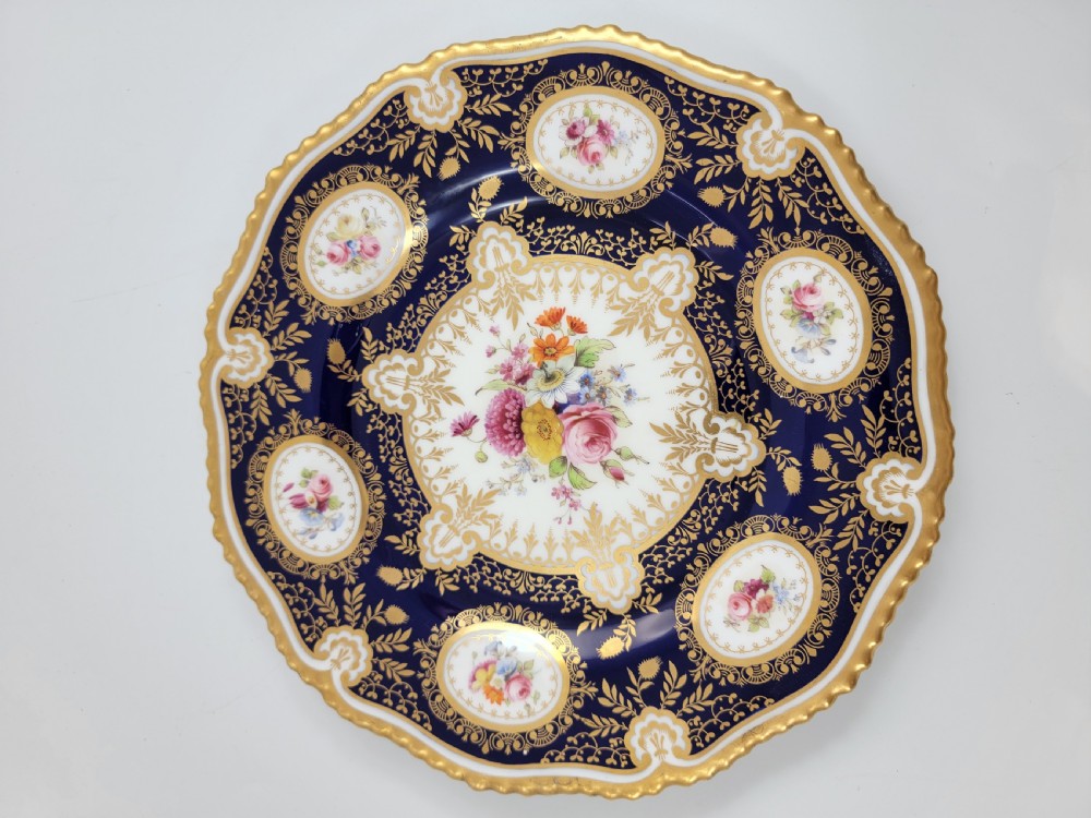 An Edwardian Royal Worcester circular porcelain cabinet plate with a cobalt blue rim decorated in heavy tooled gilding and six small floral cartouches surrounding a central hand-painted bouquet. View VI