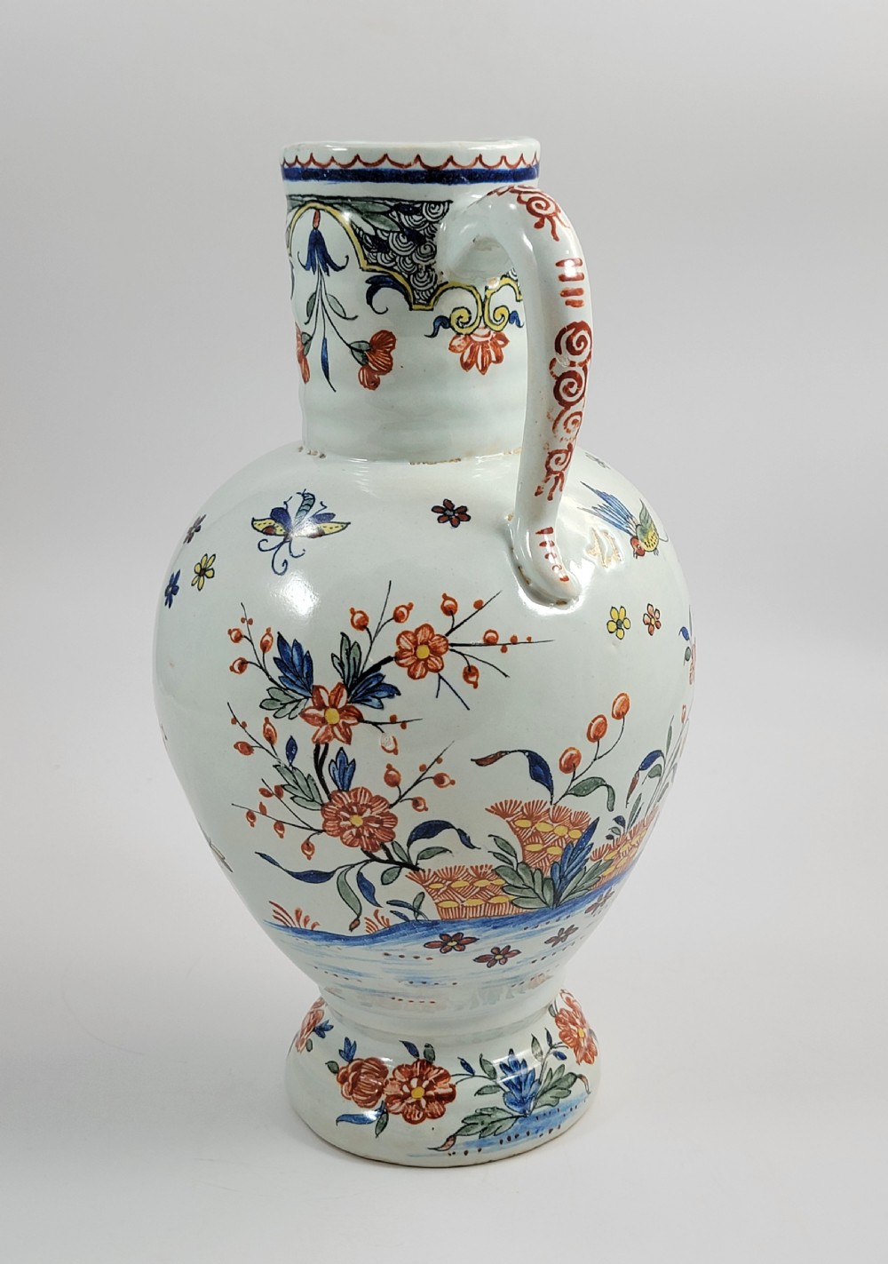 An eighteenth-century tin-glazed earthenware jug featuring a moulded mask spout, loop handle, and hand-painted polychrome floral and bird motifs on a white background. View III