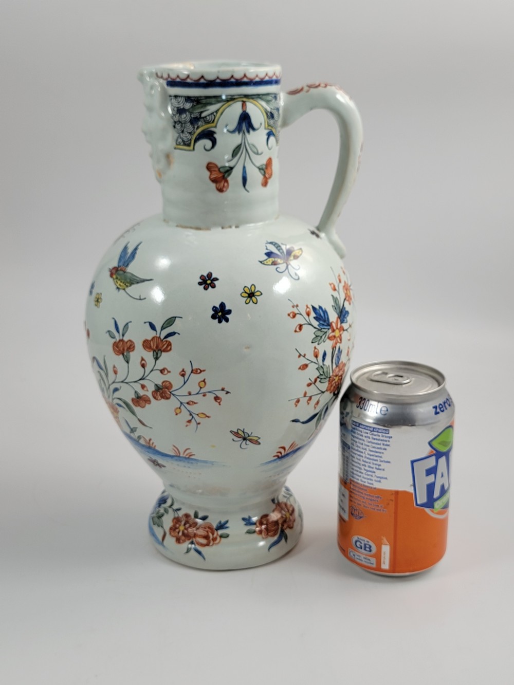 An eighteenth-century tin-glazed earthenware jug featuring a moulded mask spout, loop handle, and hand-painted polychrome floral and bird motifs on a white background. View XIV