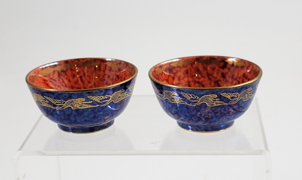 A pair of small Wedgwood lustre porcelain bowls featuring a cobalt blue exterior decorated with gilt birds and a mottled orange interior.