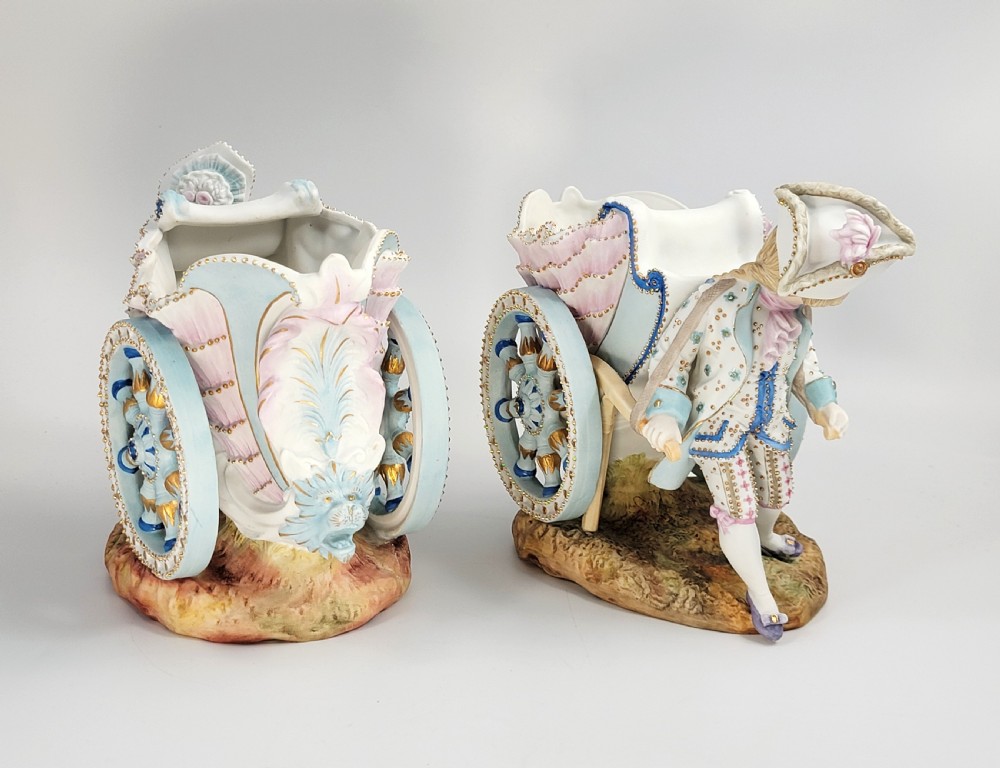A pair of late 19th-century German hand-painted porcelain figural flower carts featuring a male and female figure in 18th-century attire pulling gilded two-wheeled carriages. View IV