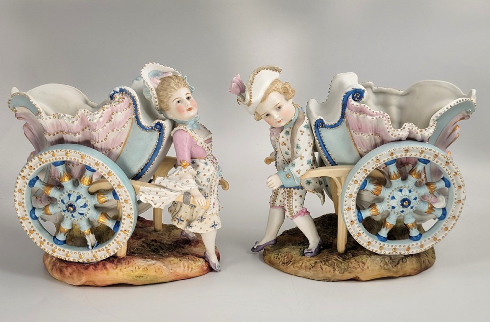 A pair of late 19th-century German hand-painted porcelain figural flower carts featuring a male and female figure in 18th-century attire pulling gilded two-wheeled carriages. View VI