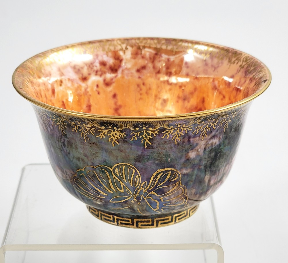 A circular porcelain bowl featuring a mottled iridescent purple exterior decorated with gilt butterfly motifs and a gold-toned orange interior.