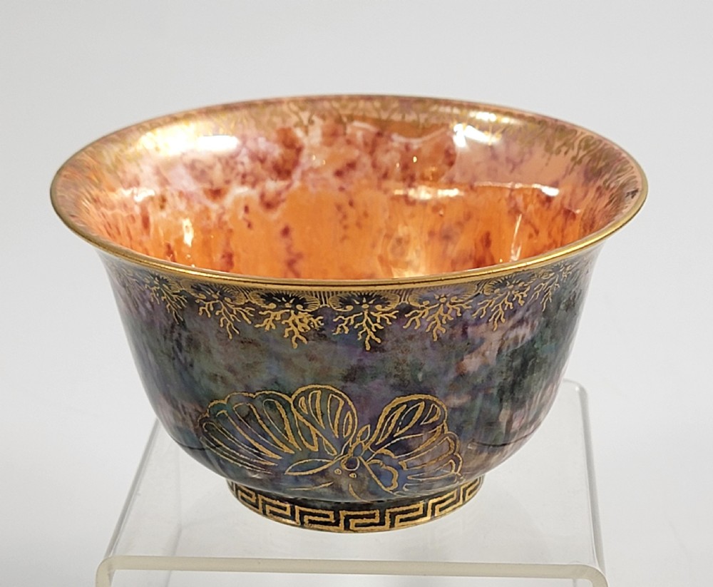 A circular porcelain bowl featuring a mottled iridescent purple exterior decorated with gilt butterfly motifs and a gold-toned orange interior. View VI