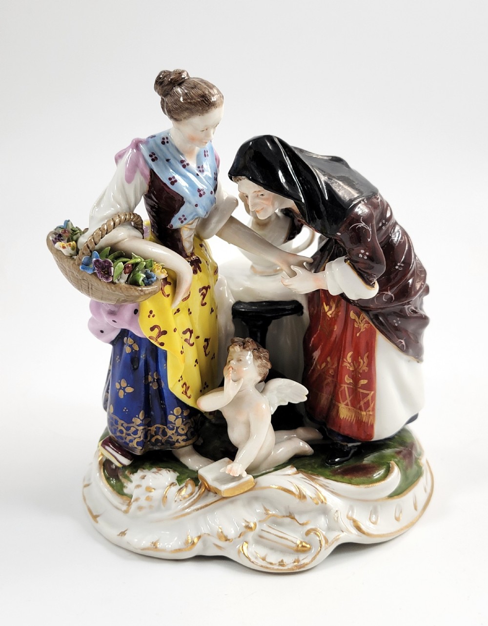 A hand-painted Volkstedt porcelain figural group featuring a fortune teller reading a young womans palm with a small winged cupid figure below.