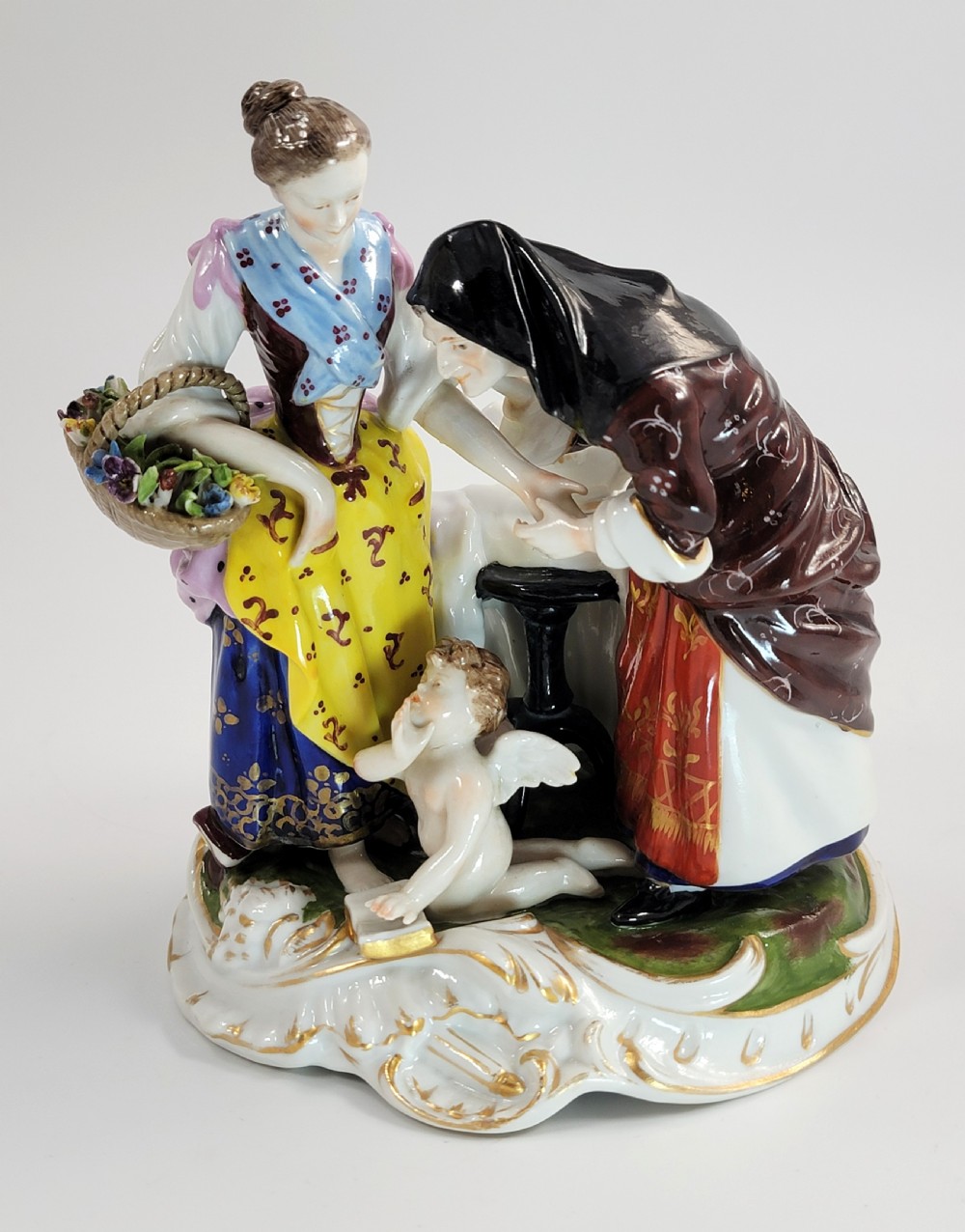 A hand-painted Volkstedt porcelain figural group featuring a fortune teller reading a young womans palm with a small winged cupid figure below. View II