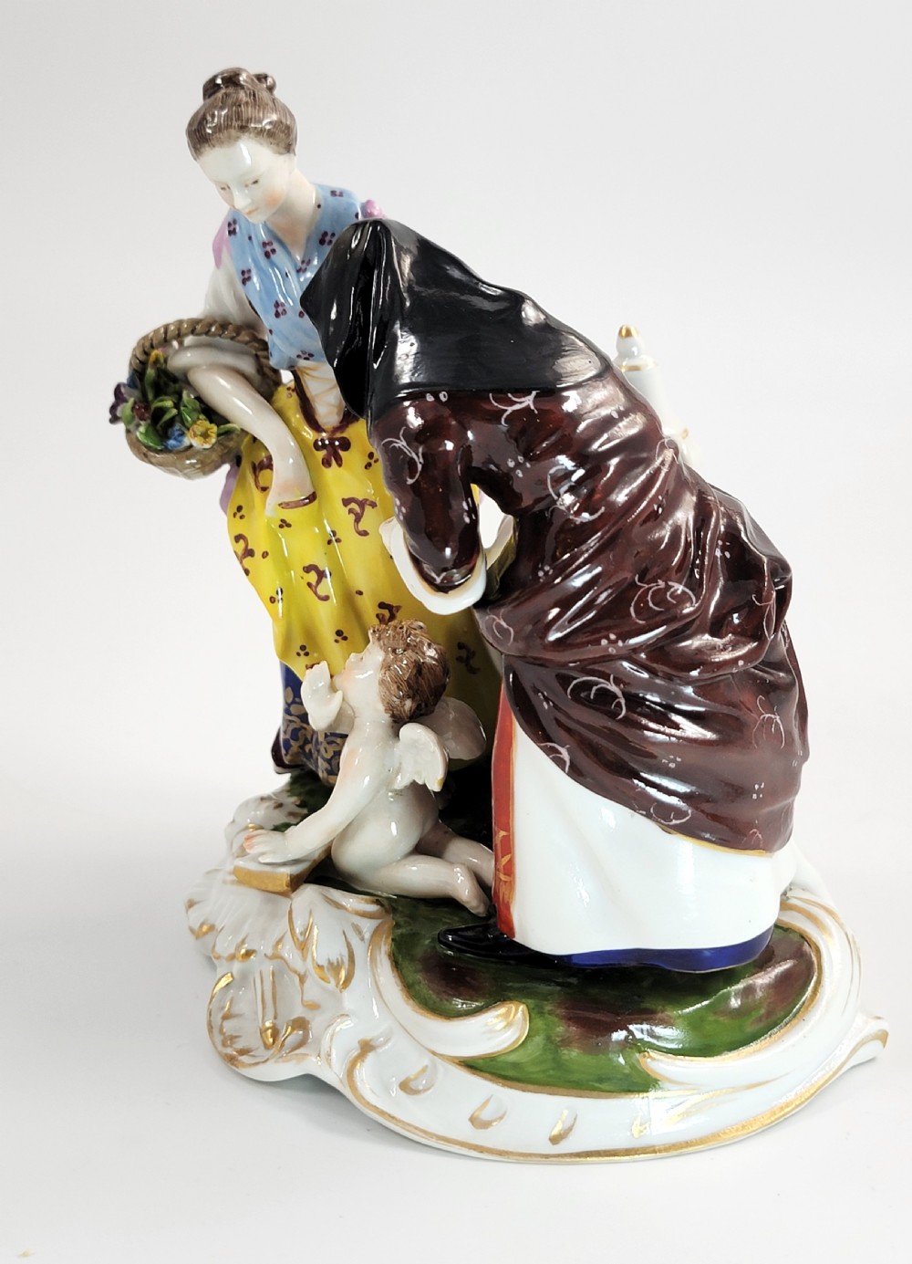 A hand-painted Volkstedt porcelain figural group featuring a fortune teller reading a young womans palm with a small winged cupid figure below. View IV