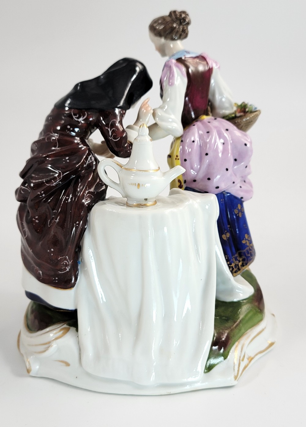 A hand-painted Volkstedt porcelain figural group featuring a fortune teller reading a young womans palm with a small winged cupid figure below. View V