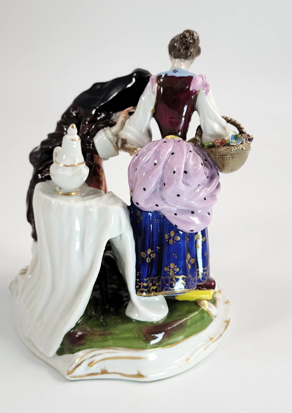 A hand-painted Volkstedt porcelain figural group featuring a fortune teller reading a young womans palm with a small winged cupid figure below. View VI