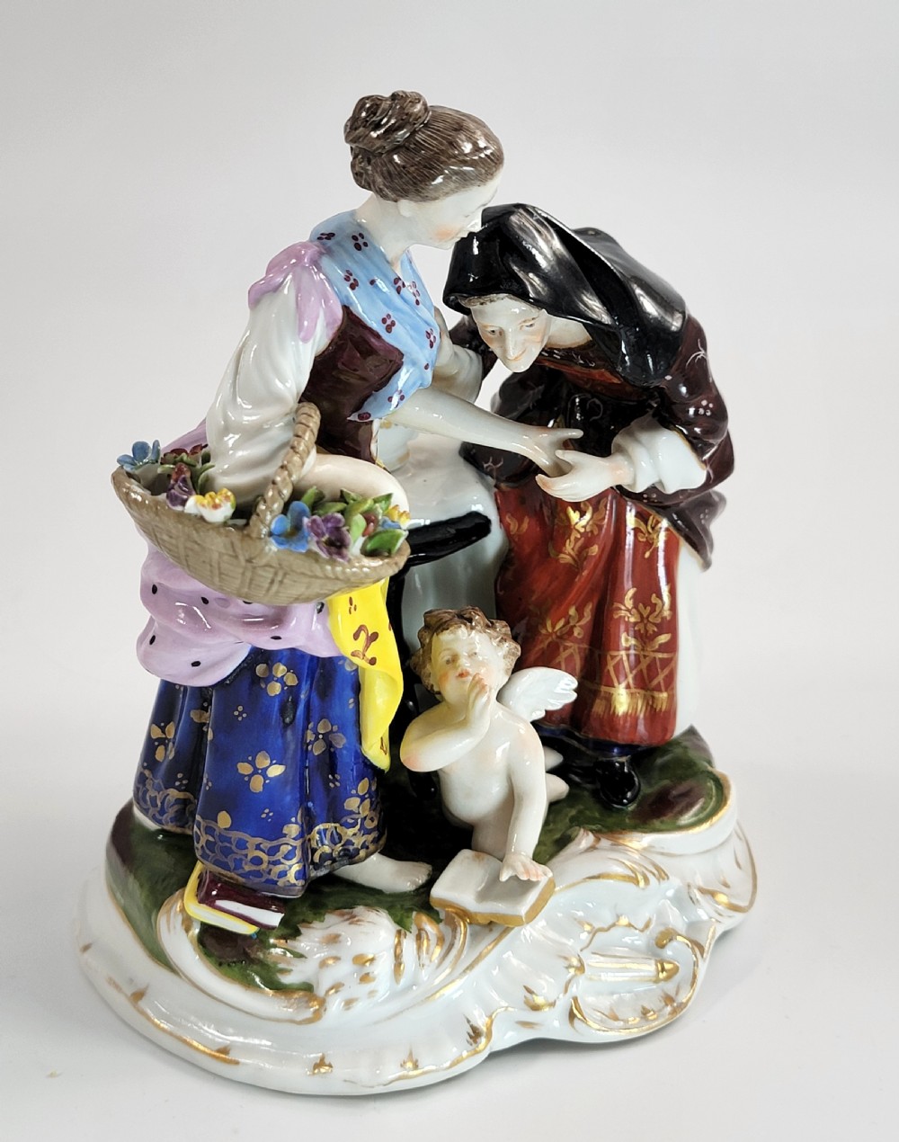 A hand-painted Volkstedt porcelain figural group featuring a fortune teller reading a young womans palm with a small winged cupid figure below. View VIII