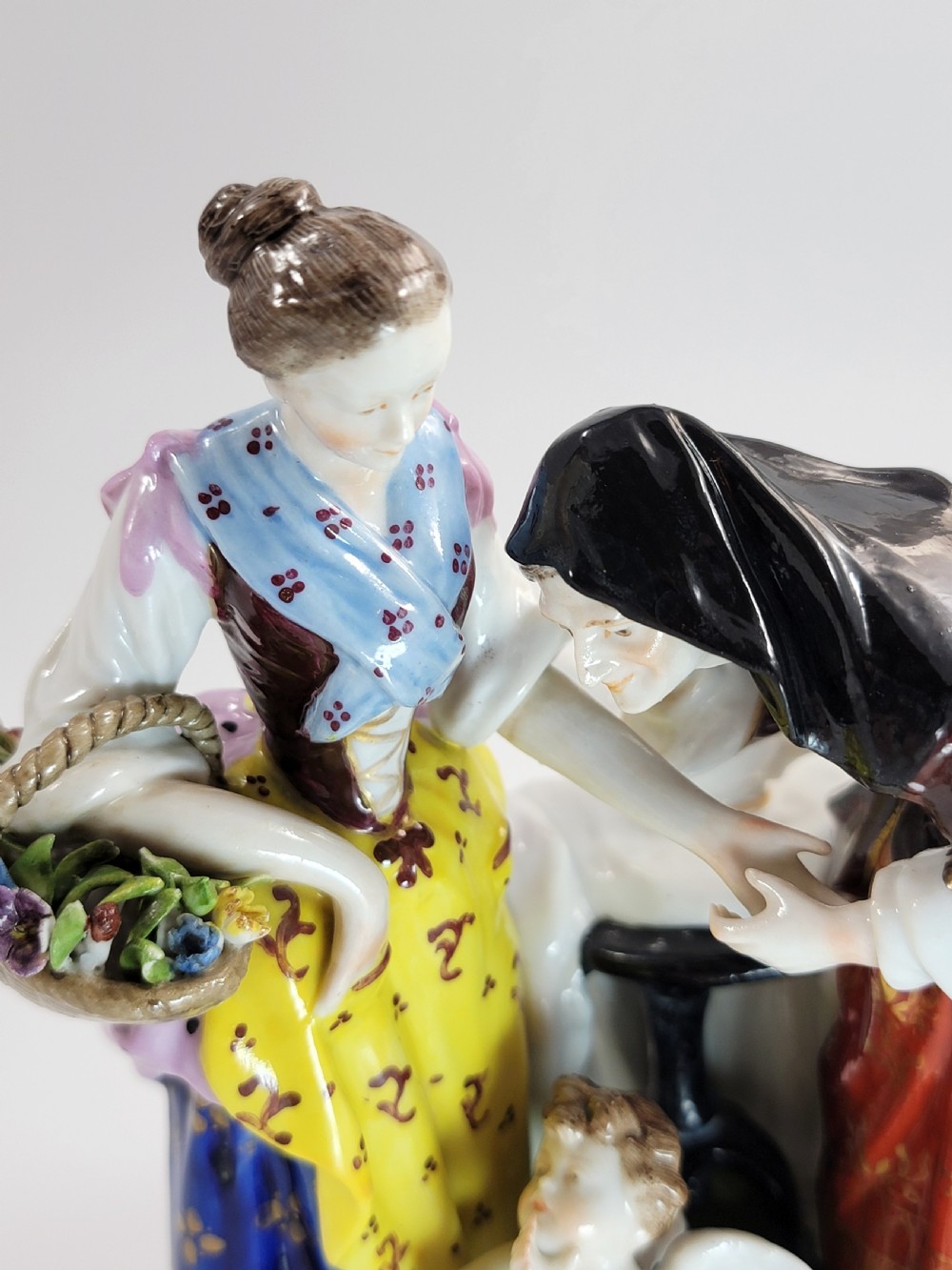 A hand-painted Volkstedt porcelain figural group featuring a fortune teller reading a young womans palm with a small winged cupid figure below. View IX