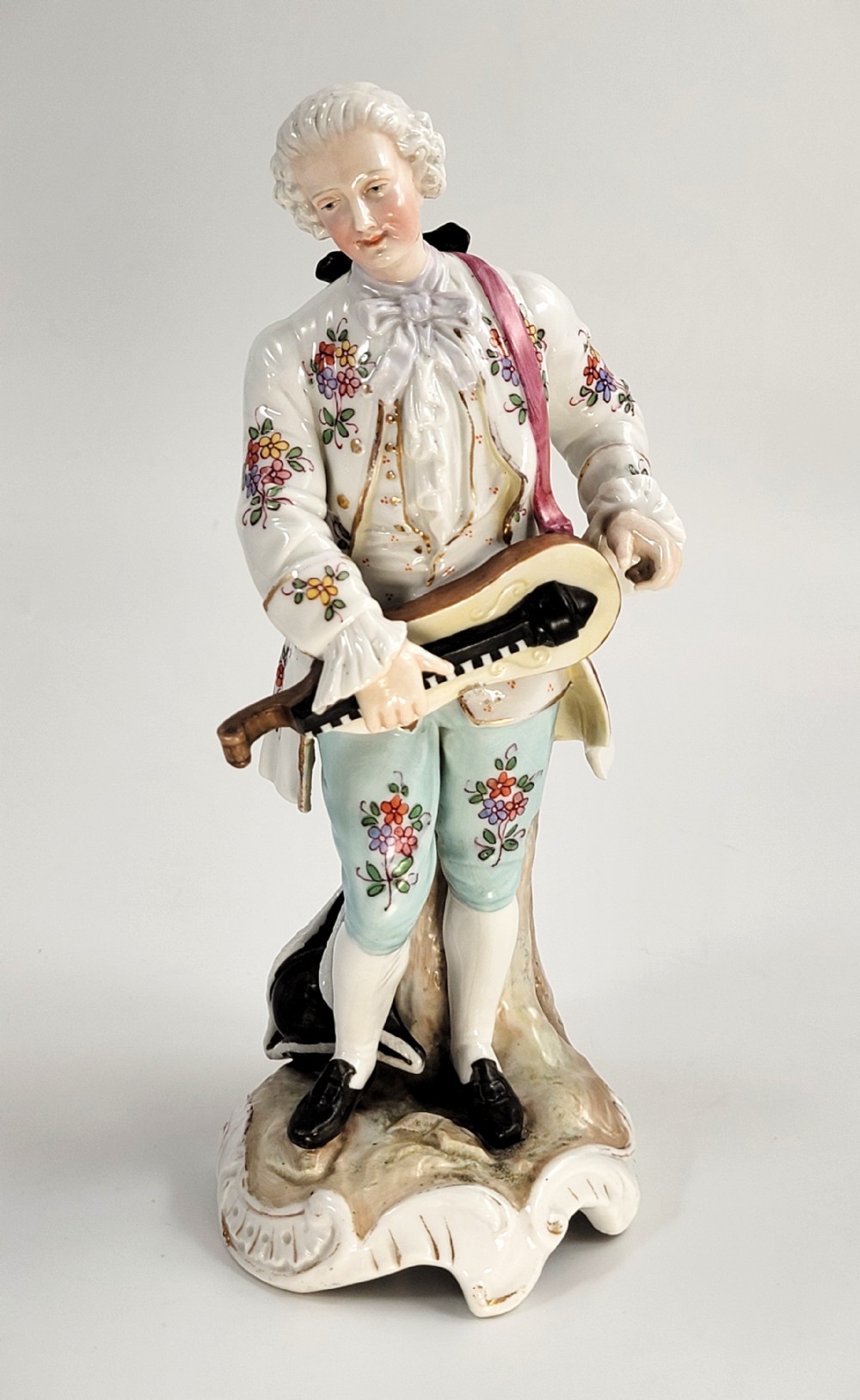 A Samson of Paris porcelain figure depicting an eighteenth-century male musician holding a hurdy-gurdy, decorated with hand-painted floral motifs and gilding.