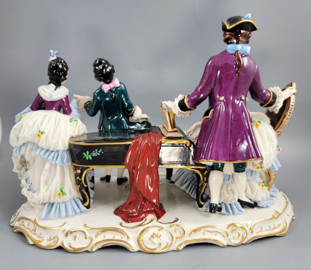 A German porcelain figural group depicting four 18th-century courtly figures around a grand piano with detailed porcelain lace dresses on a black wooden base. View VII