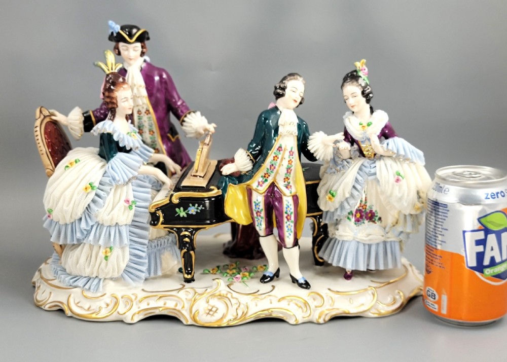 A German porcelain figural group depicting four 18th-century courtly figures around a grand piano with detailed porcelain lace dresses on a black wooden base. View XV