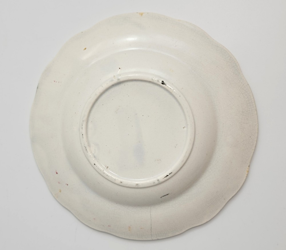 A circular Victorian ceramic plate featuring a central black transfer print of the Battle of Tchernaya surrounded by a scalloped rim with green, red, and yellow enamel accents. View III