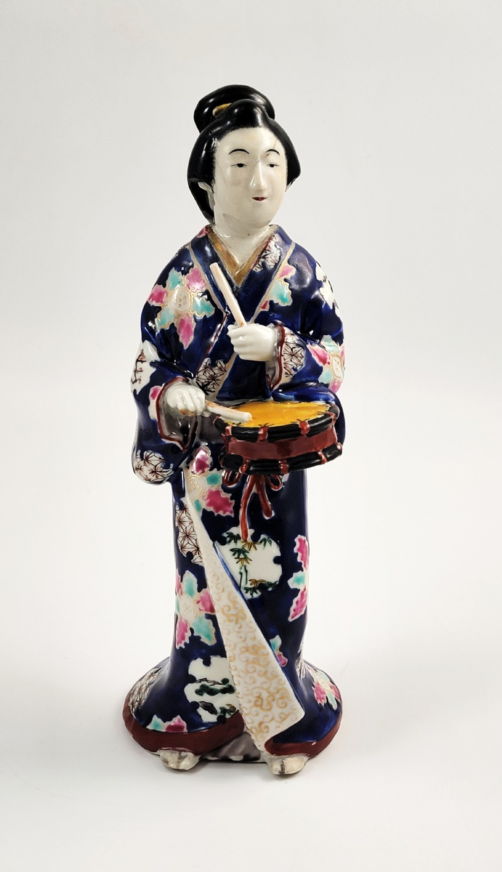 Japanese Kutani porcelain figurine of a standing lady in a cobalt blue floral kimono playing a hand drum.