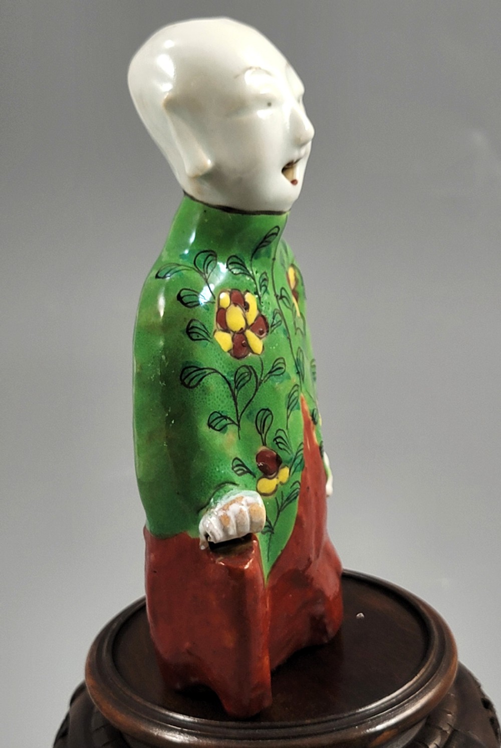 An antique Chinese ceramic incense holder depicting a smiling boy in a green floral jacket seated on a red base. View III