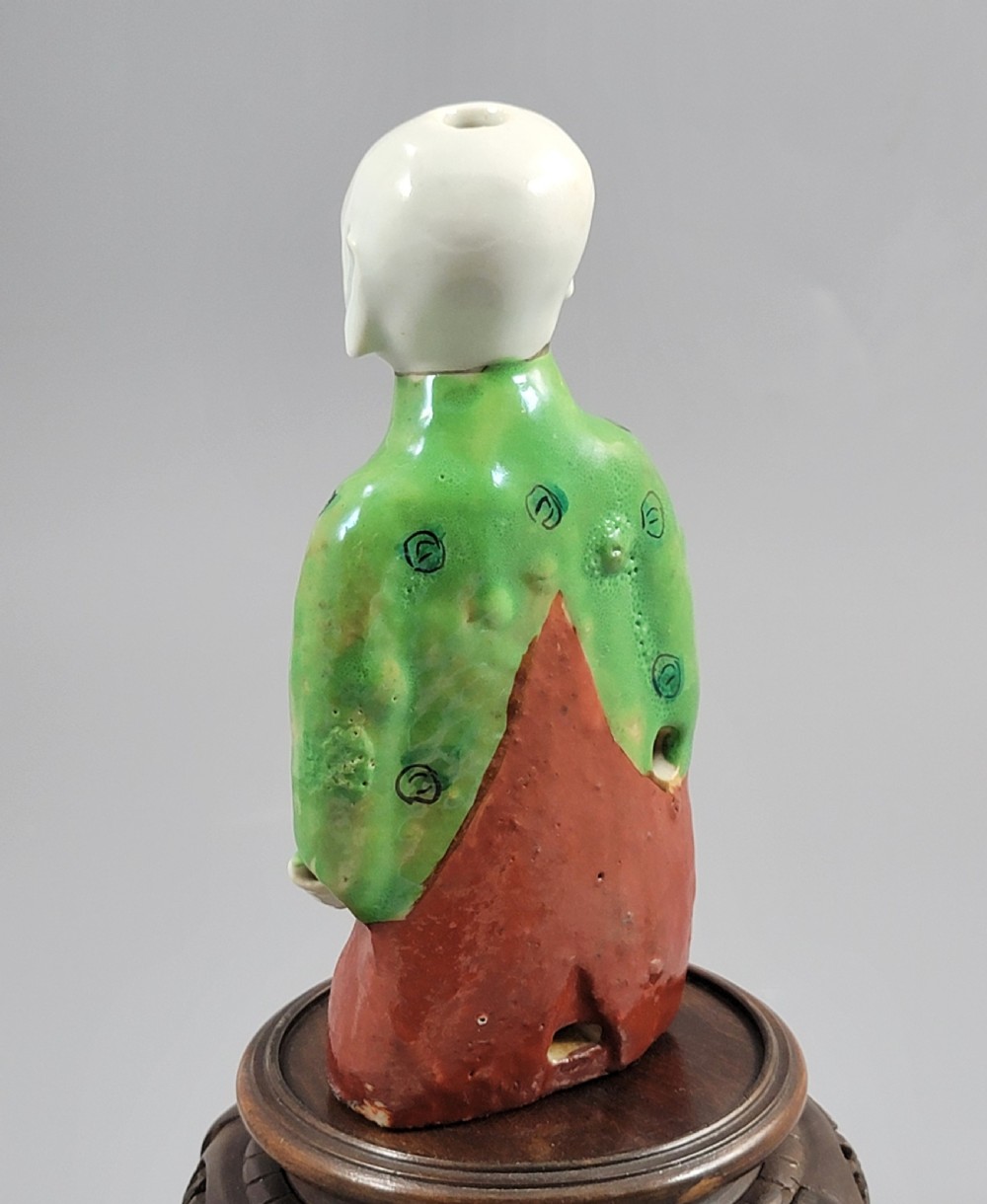 An antique Chinese ceramic incense holder depicting a smiling boy in a green floral jacket seated on a red base. View V