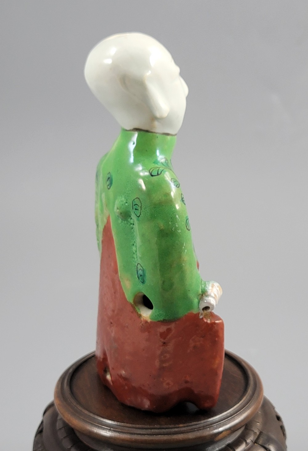 An antique Chinese ceramic incense holder depicting a smiling boy in a green floral jacket seated on a red base. View VI