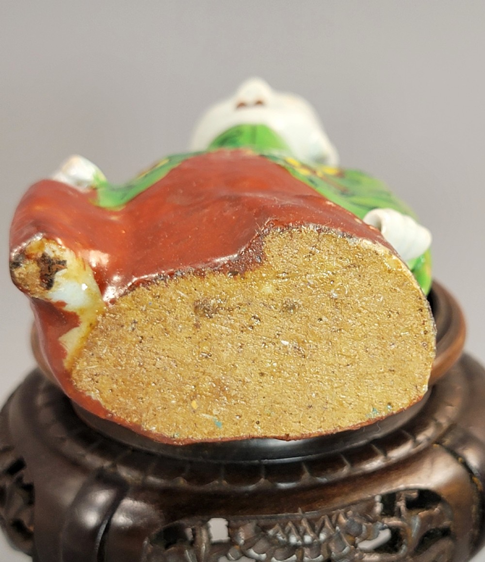 An antique Chinese ceramic incense holder depicting a smiling boy in a green floral jacket seated on a red base. View VIII