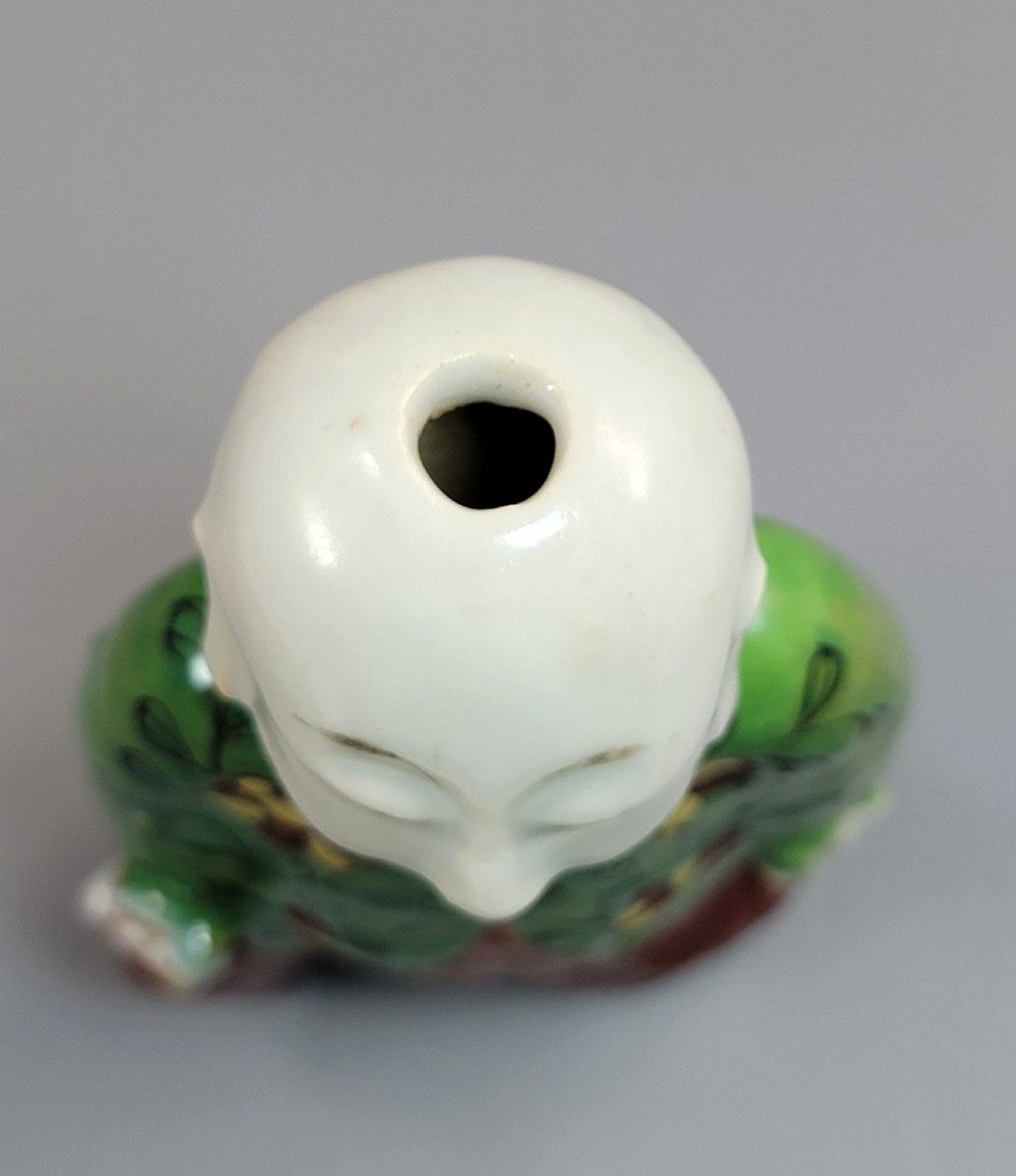 An antique Chinese ceramic incense holder depicting a smiling boy in a green floral jacket seated on a red base. View IX