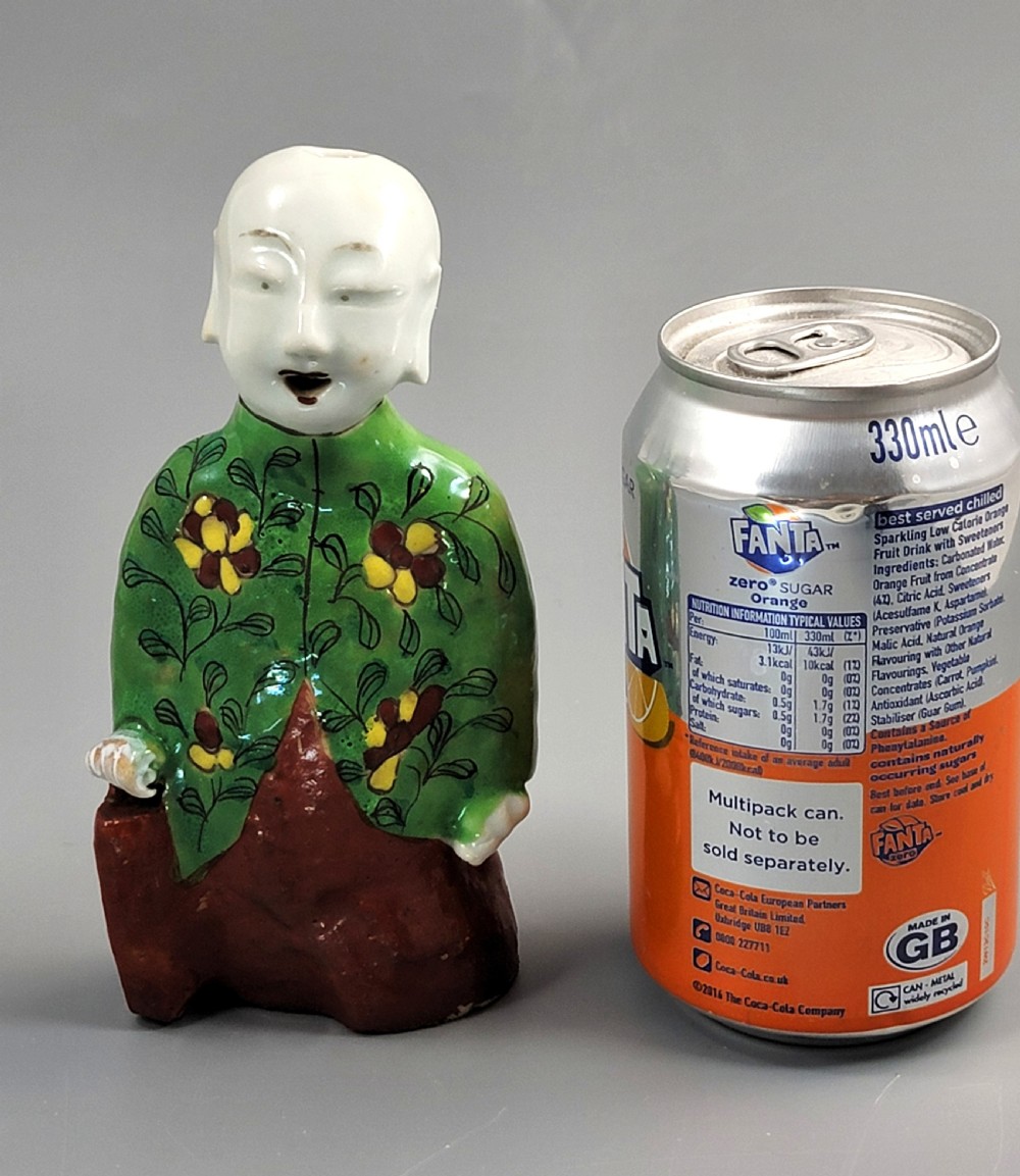An antique Chinese ceramic incense holder depicting a smiling boy in a green floral jacket seated on a red base. View X
